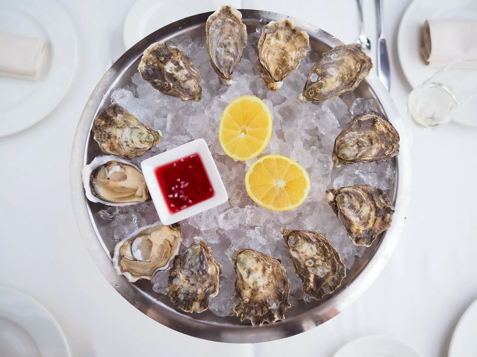A platter of fresh oysters on ice with lemon slices and red sauce, served elegantly.
